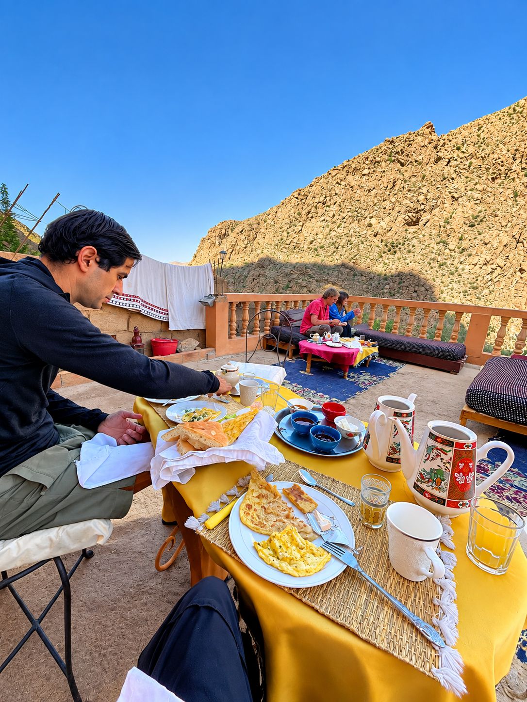 An outdoor dining area with a table set for breakfast, including plates of food, cups, and a teapot.