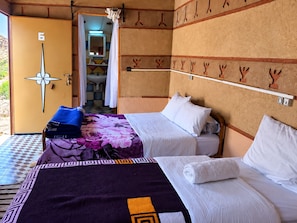 Una habitación con dos camas, un baño visible a través de una puerta abierta y un perchero en la pared.