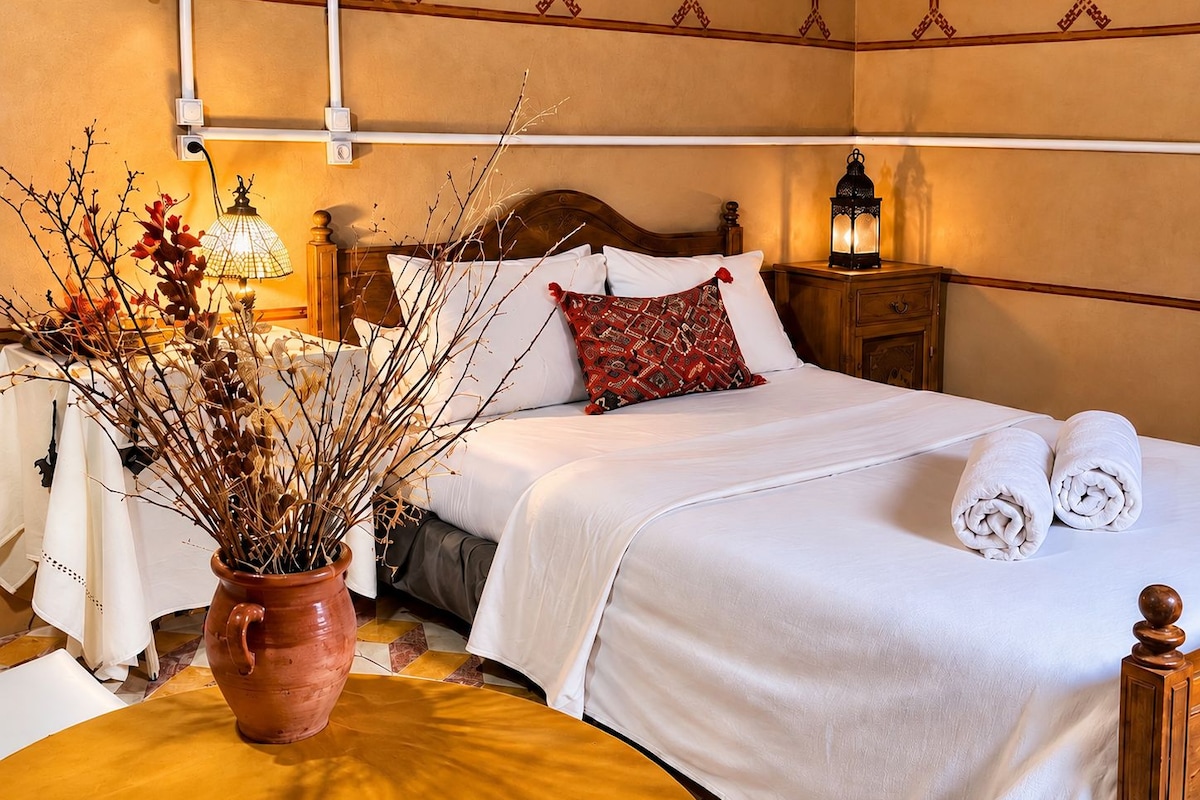 A hotel room with a bed, bedside table, lamp, and decorative vase.