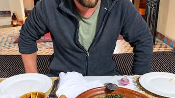Um homem sentado à mesa com uma refeição, um chão estampado e um muro decorativo.