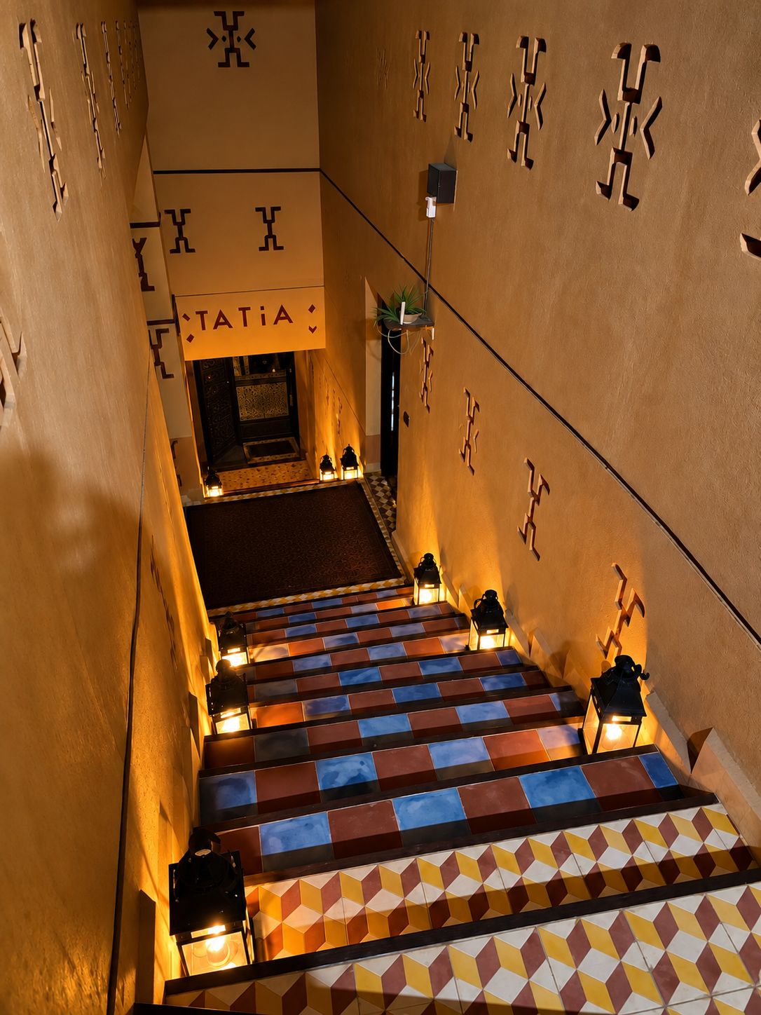 A staircase with geometric patterned tiles leading to a room with a checkered floor and a sign reading 'TATIANA'.