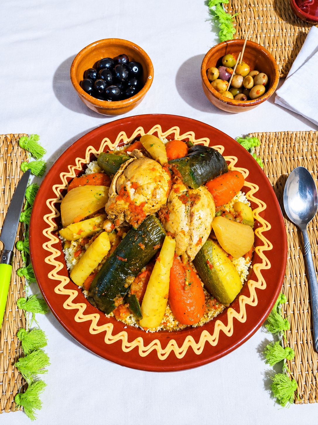 A plate of food with vegetables and a chicken leg, accompanied by two bowls of olives.