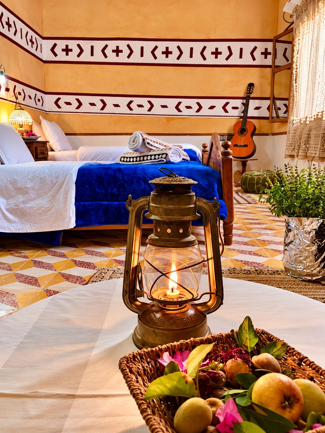 A room with a bed, a guitar, a lantern, and a basket of fruit.