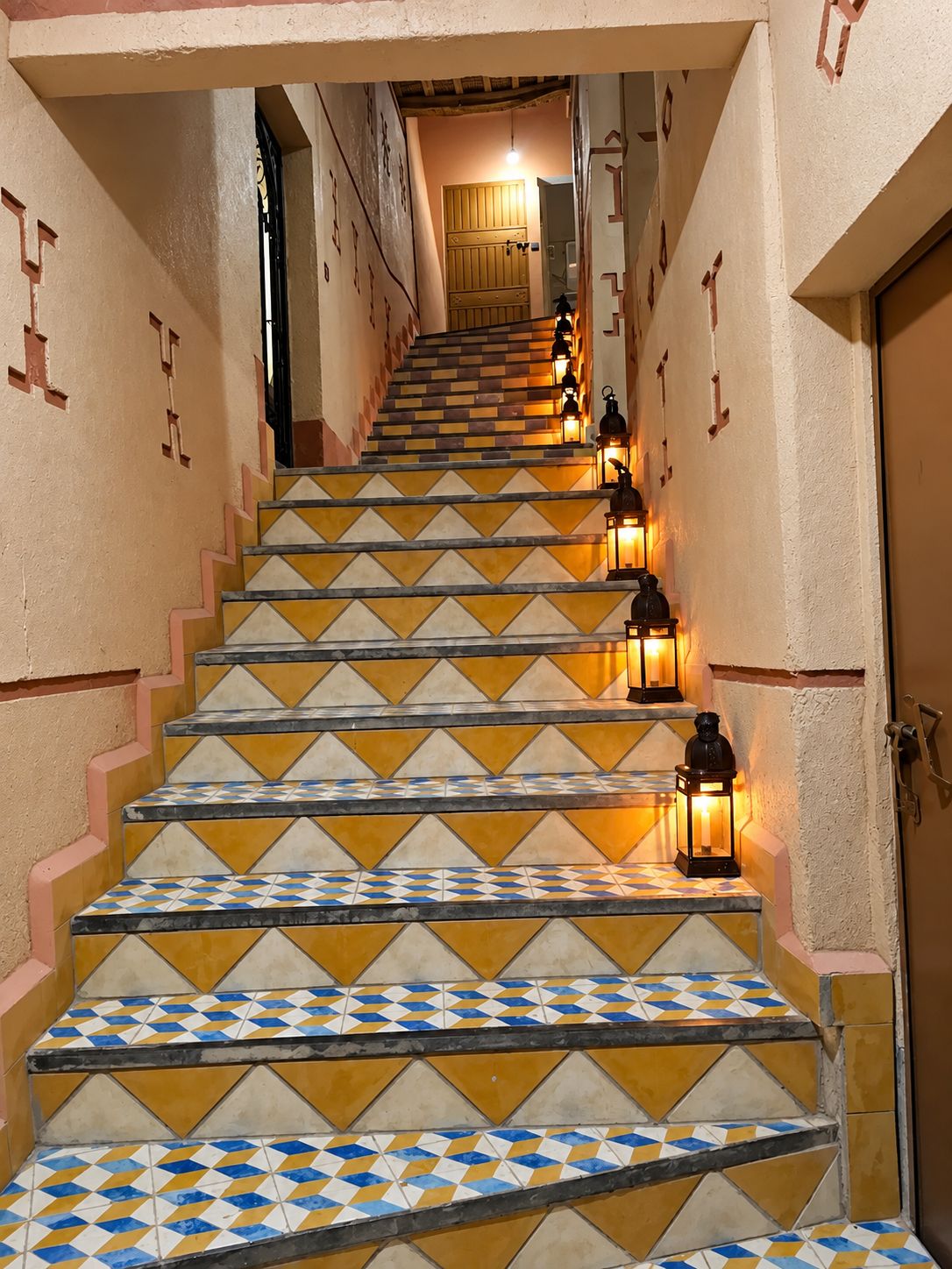 Una escalera con baldosas estampadas y faroles fijados a la pared.