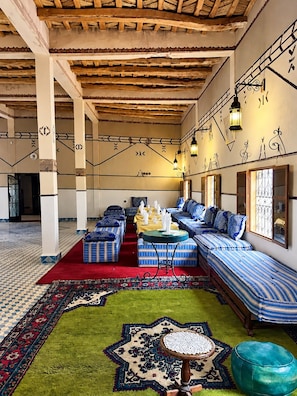 A traditional interior with a long sofa set, patterned rugs, and a wooden ceiling.