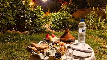 An outdoor dining setup with a table, food, a water bottle, and a traditional clay pot.