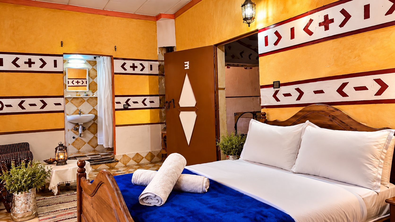 Habitación de hotel con cama, mesita de noche, espejo, lavamanos y puerta con señalización.