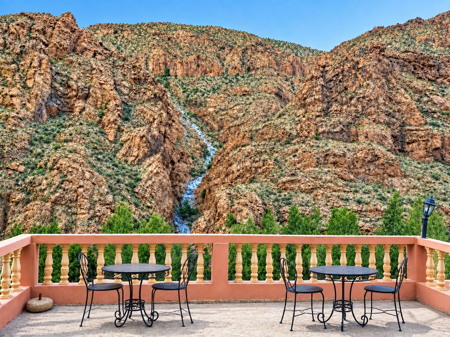 Eine Terrasse mit Tischen und Stühlen mit Blick auf eine gebirgige Landschaft und einen Bach.
