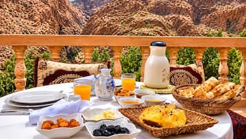Mesa posta para o café da manhã, com diversos alimentos e vista para o terreno rochoso.