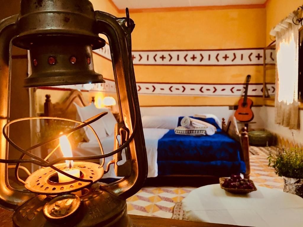 Una habitación con una cama, una guitarra, un farol y una mesita con un cuenco.