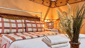 A neatly made bed with patterned bedding, a bedside table with a lamp, and a potted plant. - Hôtel panoramique de la vallée (Ait Sedrate Jbel El Soufla)