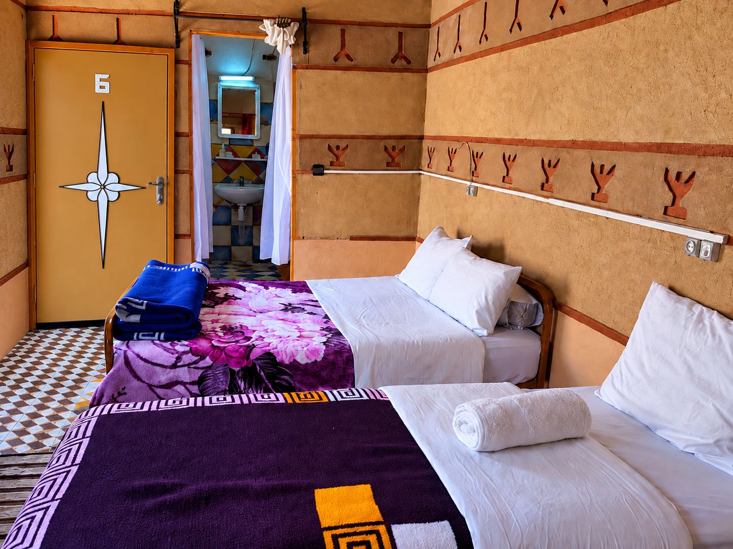 Une chambre d’hôtel avec deux lits, une salle de bain avec un lavabo et une porte portant le numéro 6.