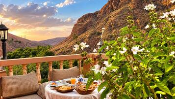 En terrass med ett bord dukat för frukost, med utsikt över ett bergigt landskap.