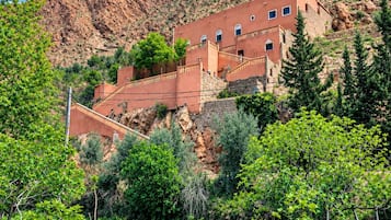 Un edificio tradicional de varios niveles, rodeado de vegetación exuberante y un paisaje montañoso.