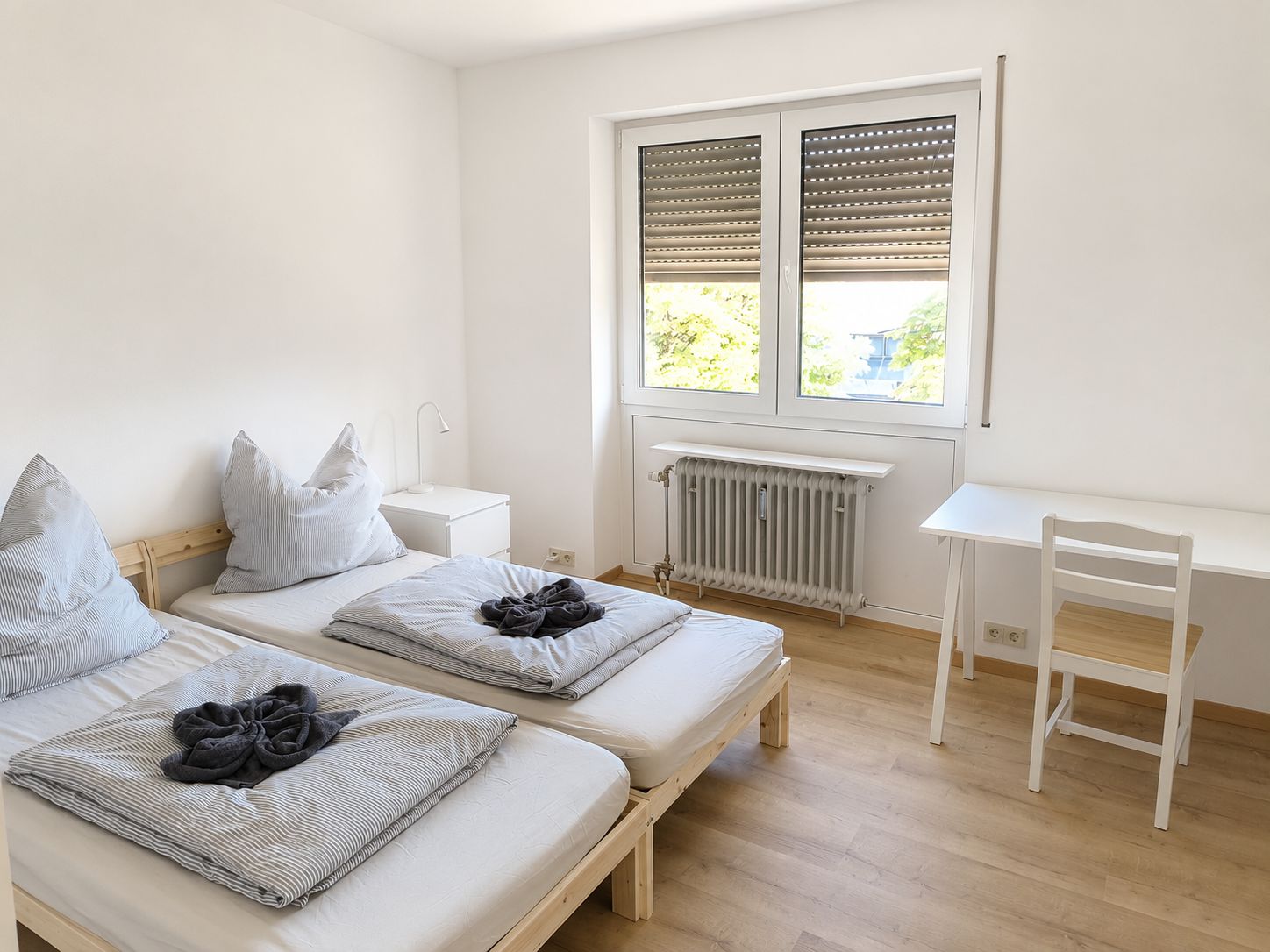 A bedroom with two beds, a desk, and a radiator.