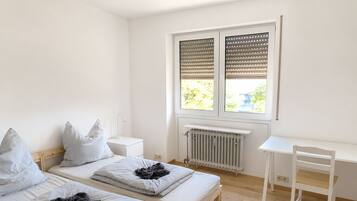 A bedroom with two beds, a desk, and a radiator.