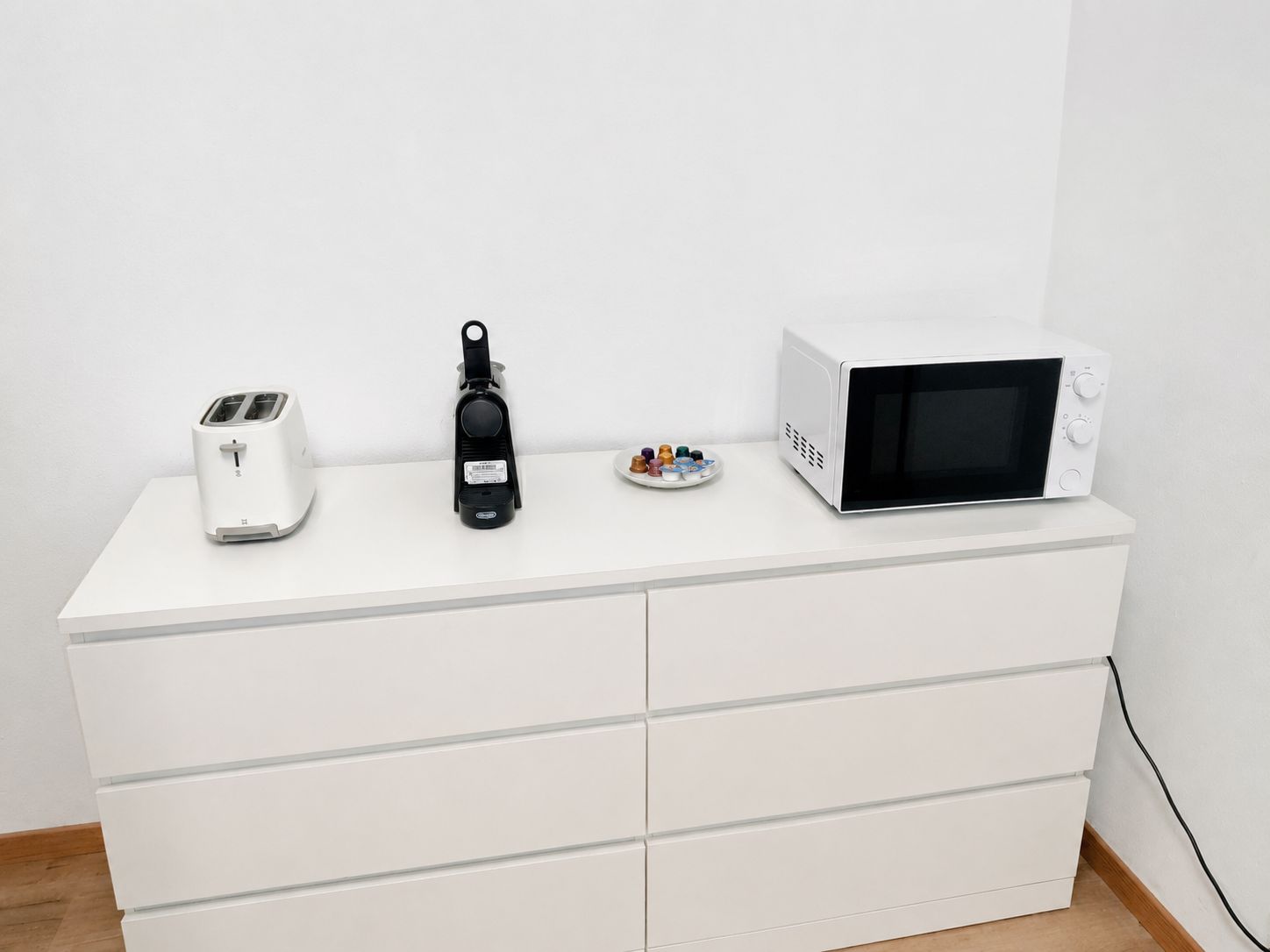 Un armario blanco con tres electrodomésticos de cocina: un tostador, una cafetera y un microondas.