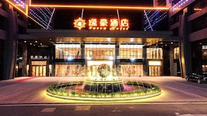 A hotel entrance with a fountain, illuminated signage, and a modern building facade. - Yucca Hotel (Jiangmen)