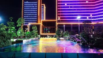 Vista nocturna de un hotel con piscina, rodeado de árboles e iluminado por luces de neón.