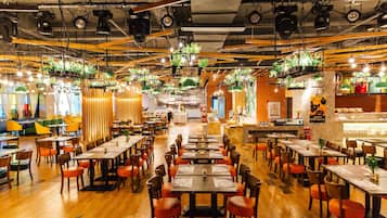 Un restaurante amplio con numerosas mesas y sillas, una zona de bar e instalaciones con plantas colgantes.
