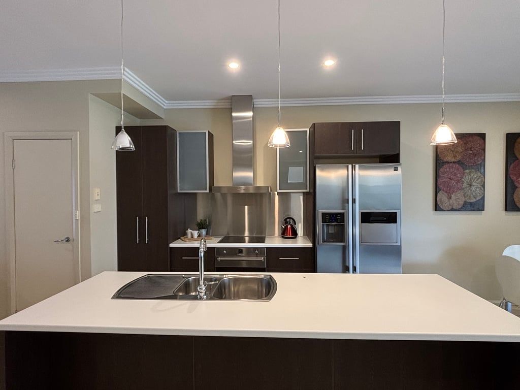 A modern kitchen with a central island, stainless steel appliances, pendant lighting, and dark cabinetry.