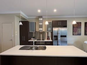 A modern kitchen with a central island, stainless steel appliances, pendant lighting, and dark cabinetry.