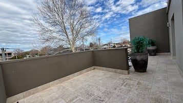 A rooftop terrace with a view of the city, a tree, and potted plants.