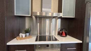 A modern kitchen with a stainless steel range hood, a built-in induction cooktop, and a stainless steel refrigerator.