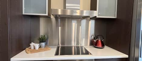 A modern kitchen with a stainless steel range hood, a built-in induction cooktop, and a stainless steel refrigerator.