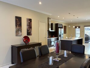 A modern kitchen with dark cabinetry, a central island, and a dining area with a dark table and chairs. - Crampton City Stay (Wagga Wagga)