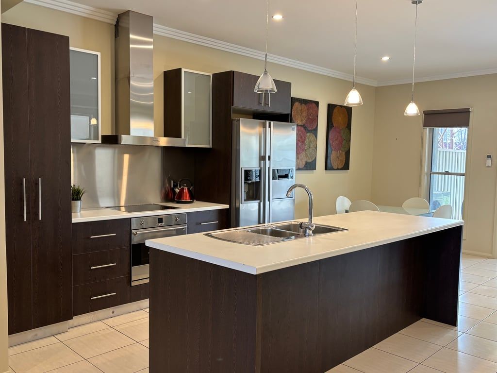 A modern kitchen with dark cabinetry, stainless steel appliances, and pendant lighting.