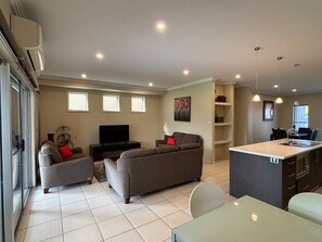 A modern living room with a sofa set, a TV, and a dining area with a kitchen island. - Crampton City Stay (Wagga Wagga)