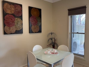 Un comedor con una mesa de vidrio, sillas blancas y dos cuadros en la pared.