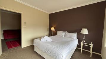 A hotel room with a bed, two bedside lamps, a red bath mat, and a door leading to a red bath.