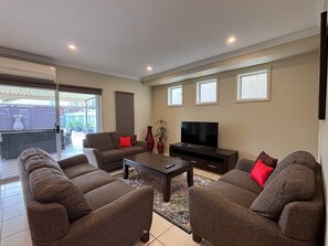 A living room with a sofa set, a coffee table, a TV, and a sliding glass door leading to an outdoor area. - Crampton City Stay (Wagga Wagga)