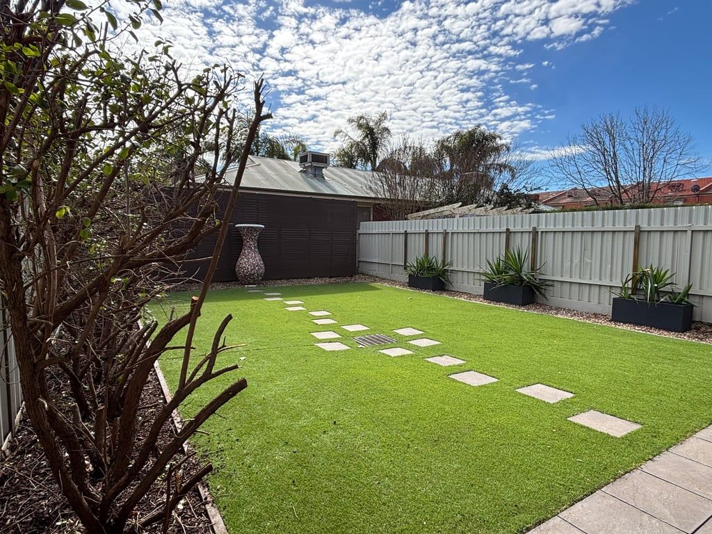 A backyard with artificial grass, a wooden fence, and a large planter.