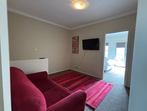 Una sala de estar con un sofá rojo, un televisor de pantalla plana montado en la pared y un tapete rojo y negro a rayas.