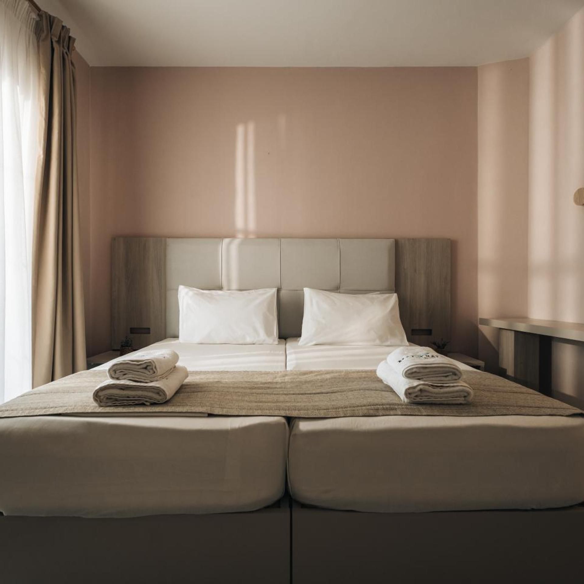 Een hotelkamer met een tweepersoonsbed, twee kussens, een nachtkastje en een raam met gordijnen.