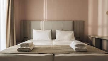 Een hotelkamer met een tweepersoonsbed, twee kussens, een nachtkastje en een raam met gordijnen.