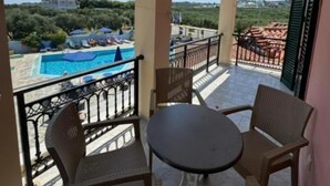 Un balcón con mesa y sillas, con vistas a una piscina y zonas verdes.
