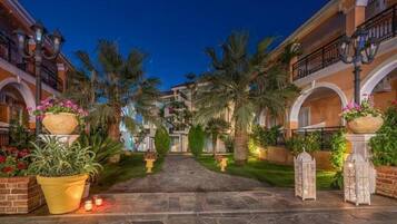 A courtyard with a stone pathway, palm trees, and potted plants.