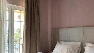 A hotel room with a bed, curtains, and a view through a door.