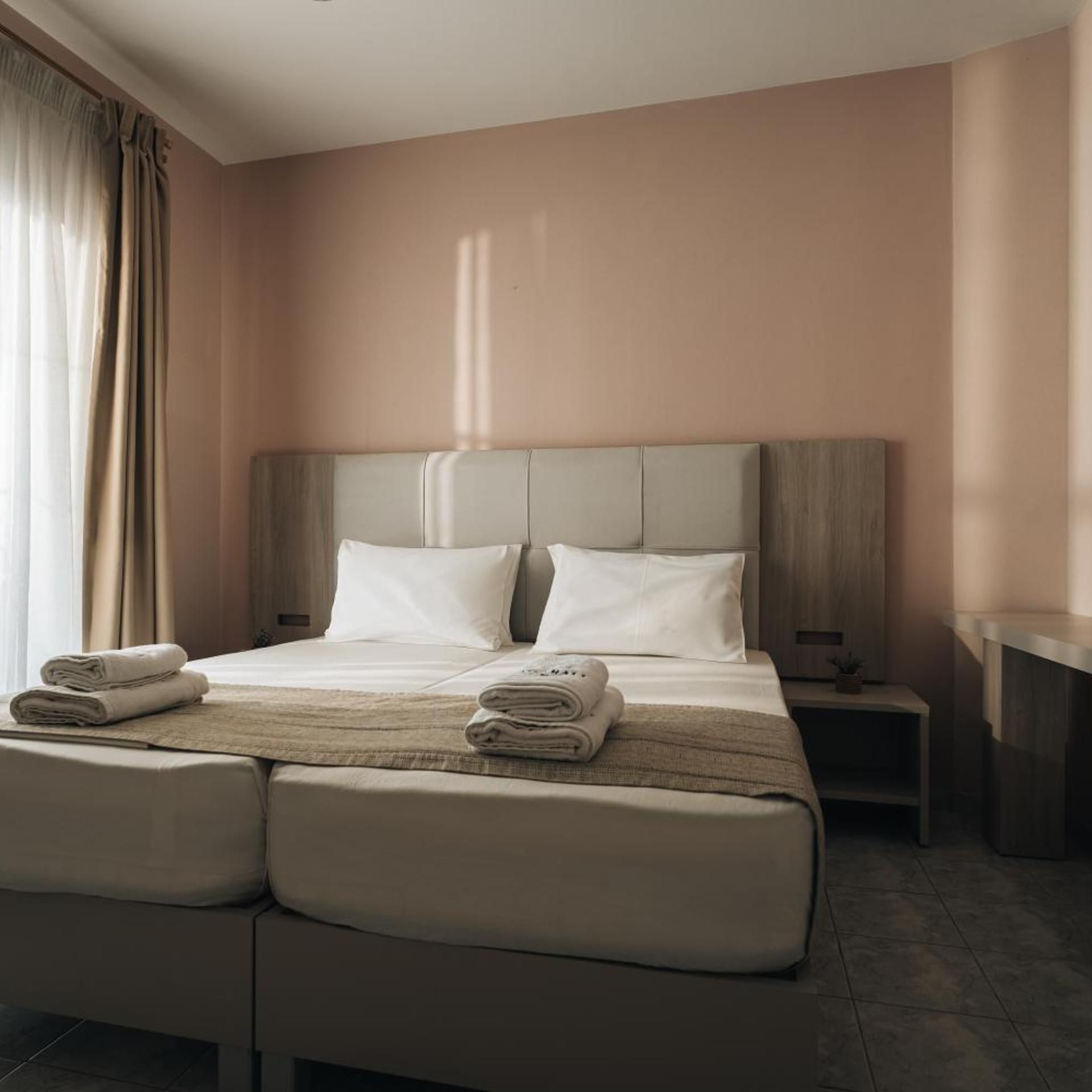 Een hotelkamer met een groot bed, twee kussens, een nachtkastje en een bijzettafeltje met een lamp.