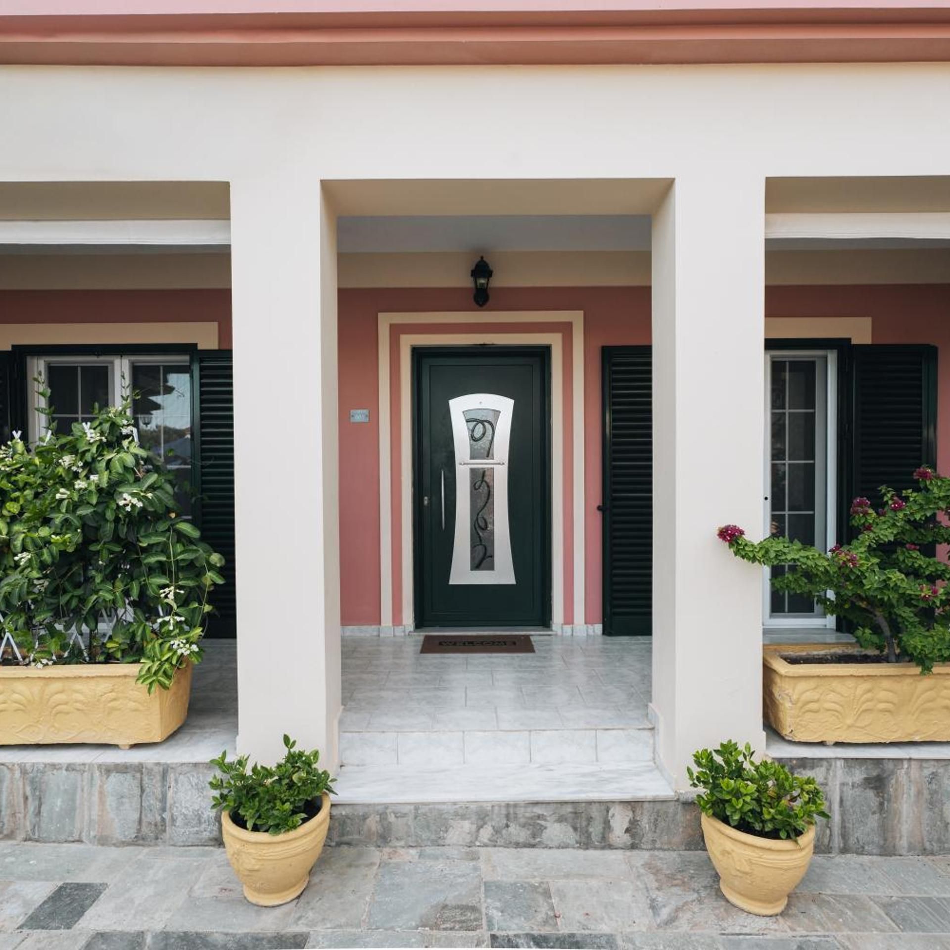 A building entrance with a central door, flanked by two potted plants, and a small step leading up to the door.