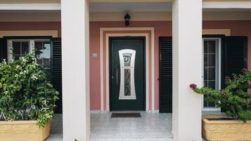A building entrance with a central door, flanked by two potted plants, and a small step leading up to the door.
