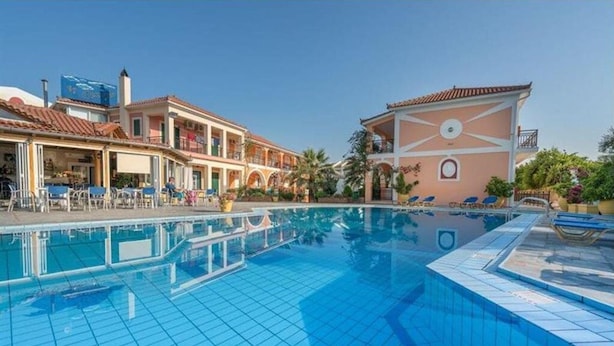 Una piscina con suelo de baldosas, junto a un edificio con varios balcones y un cielo despejado.