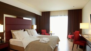 Una camera d'albergo con un letto grande, una scrivania con una sedia, una TV e una finestra con tende.