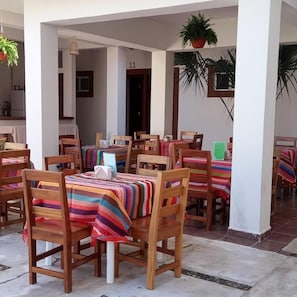 A dining area with wooden tables and chairs, striped tablecloths, and hanging plants. - Hotel Posada de Abril (Santa María Huatulco)