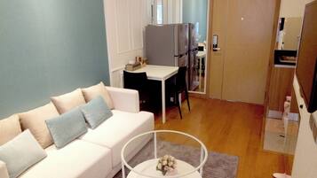 A modern living room with a white sofa, a coffee table, and a dining area with a refrigerator.