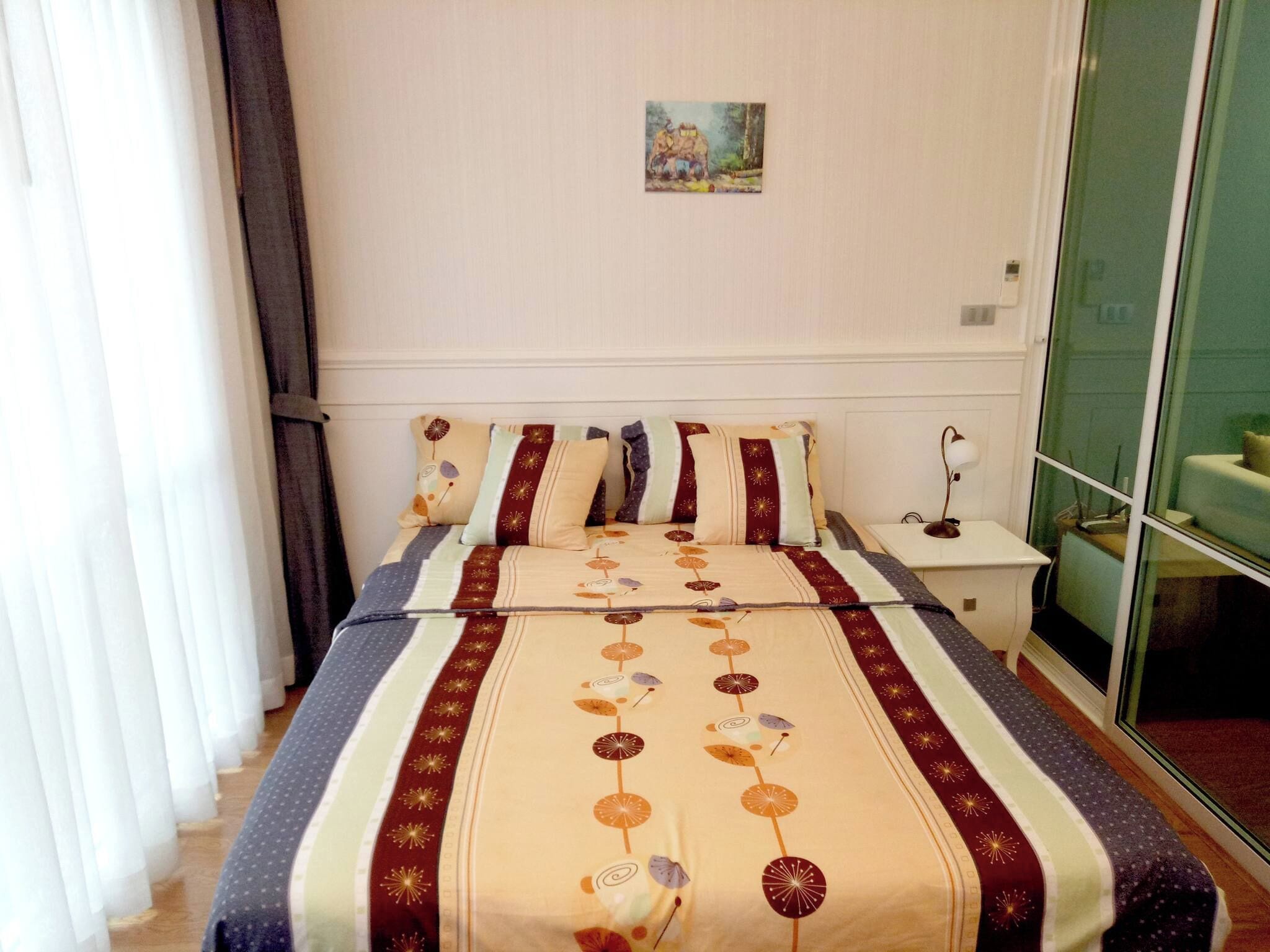 A hotel room with a bed, a nightstand, a lamp, and a painting on the wall.